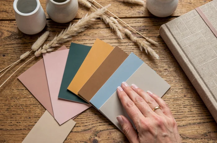 Palette de couleurs tendances 2025 en flat lay avec échantillons de peinture, céramiques et accessoires déco sur table en chêne